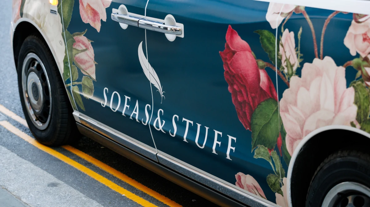 A close up of the side of a taxi which showcases a wraparound of navy blue with illustrated flowers and the words Sofas & Stuff to showcase Fox Collective's Interiors PR expertise on their home page.